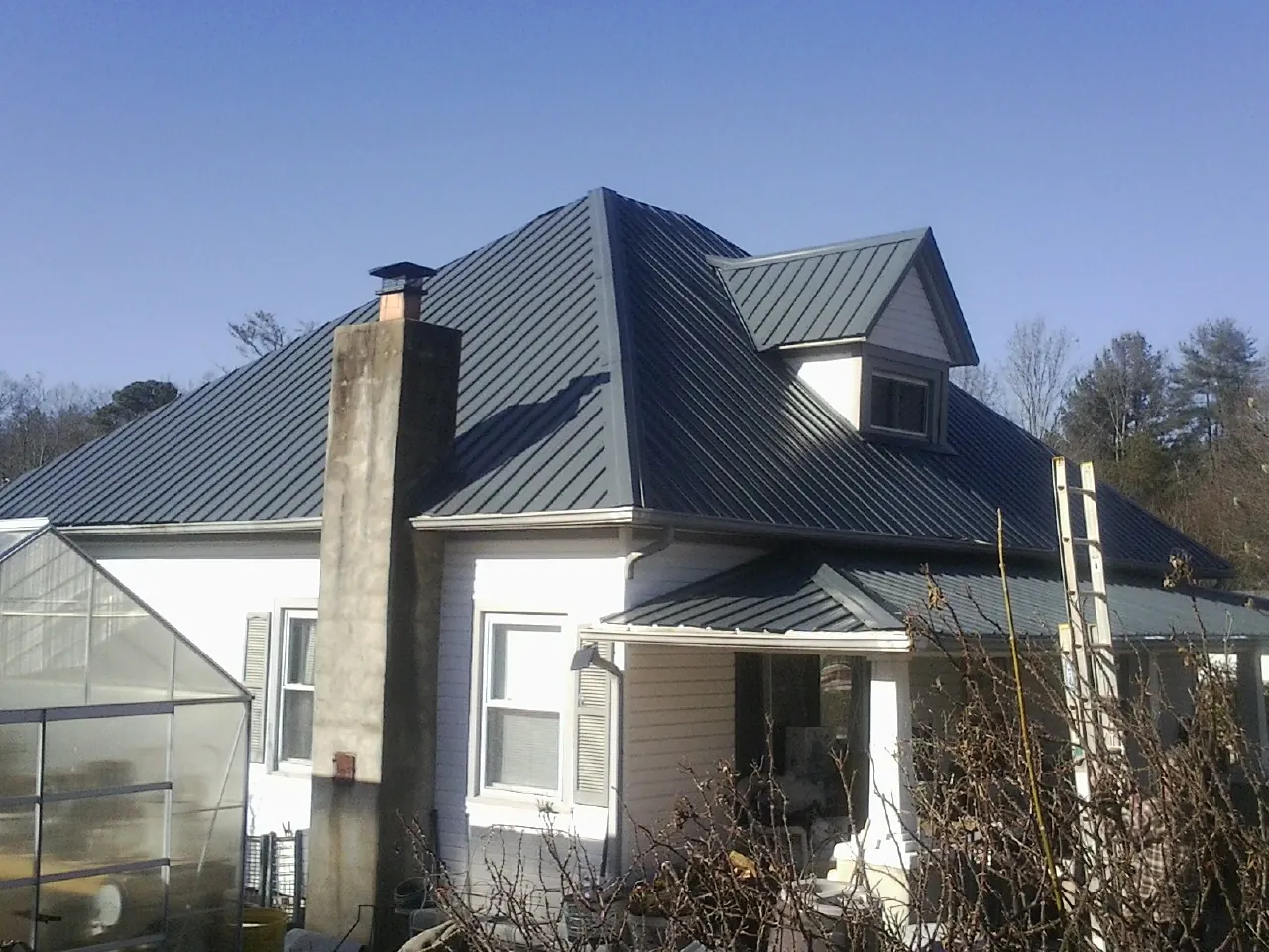 Dark blue standing seam metal roof on a white farmhouse with dormer — Slate & Tile Roof Repair by Roofing Brothers in Etowah