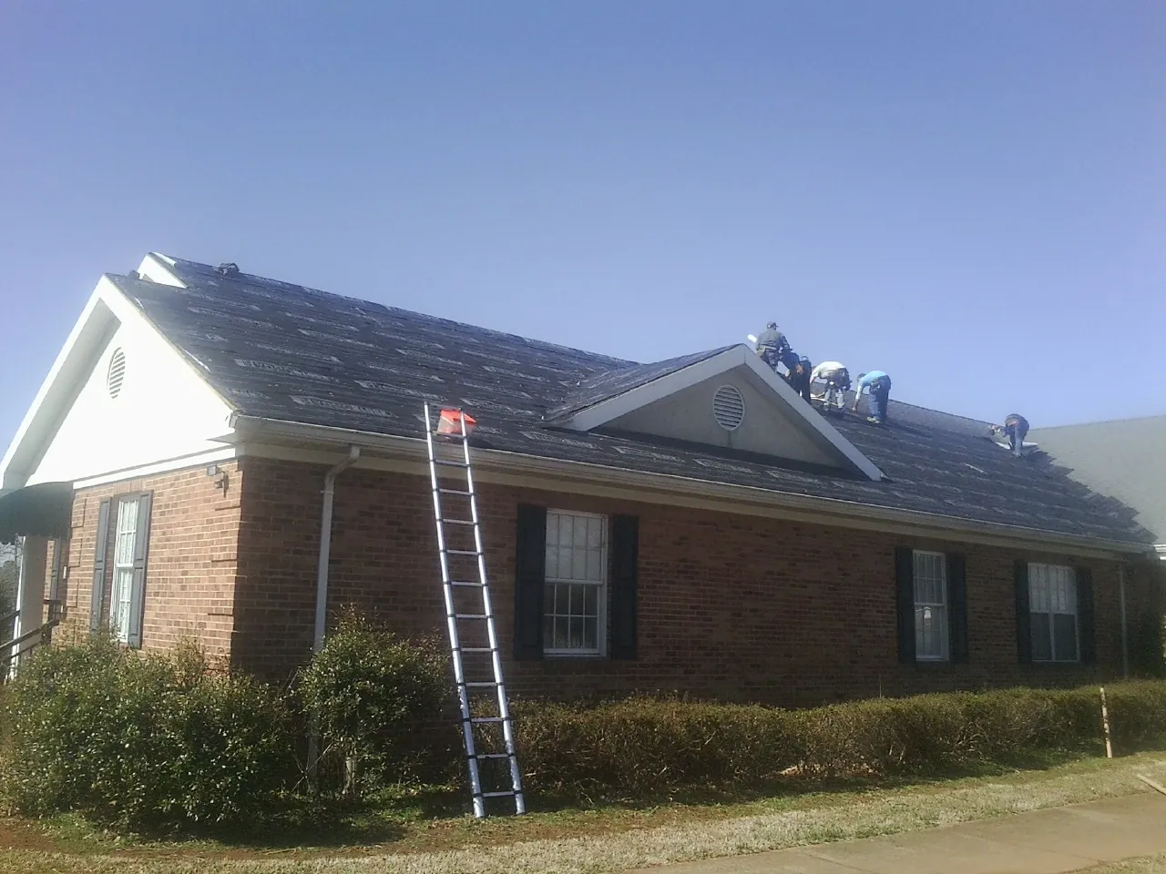Crew tearing shingles off a brick ranch roof with a ladder set — Metal Roof Repair work by our crew in Etowah