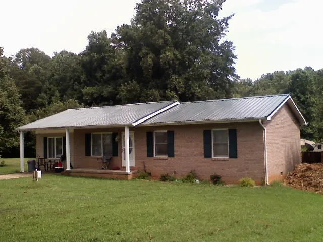 Gray metal roof on a brick ranch house with a side carport in Etowah