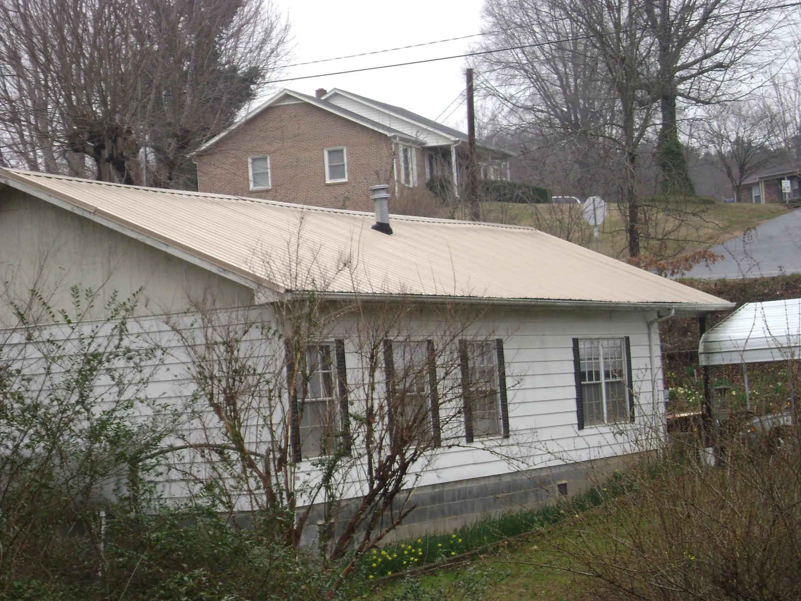 Tan metal roof on a white sided house set into a hillside — Commercial Roofing by Roofing Brothers in Etowah