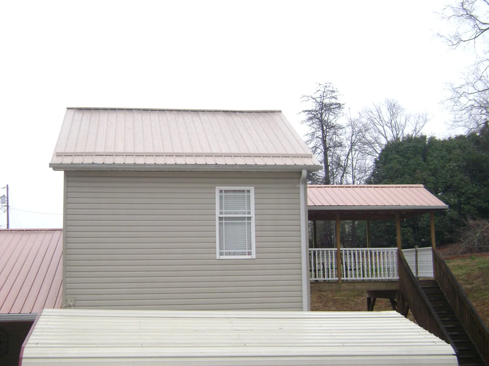 Tan metal roofs on a two story addition and attached porch, from a Roof Replacement job in Etowah
